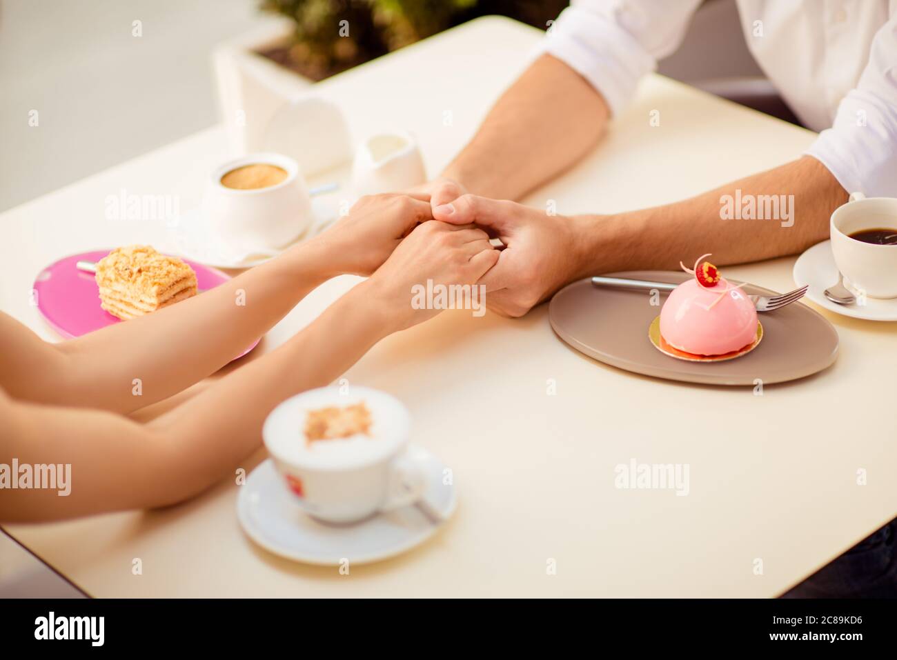 Nahaufnahme beschnittenes Foto von zwei jungen Liebenden, sitzen`s Café und halten einander die Hände, mit schönen Kaffee mit leckeren Kuchen Stockfoto